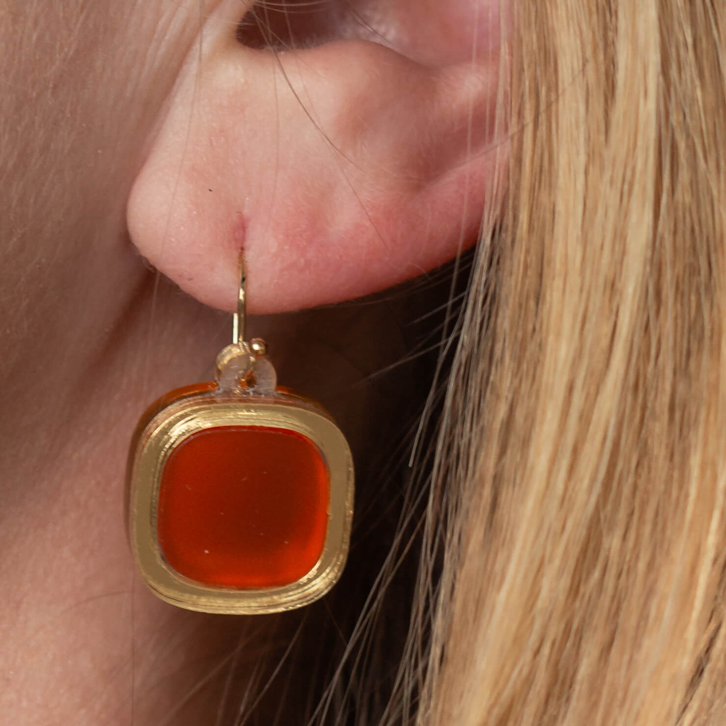 Close-up of model’s ear wearing frosted small wire earrings in mandarin orange
