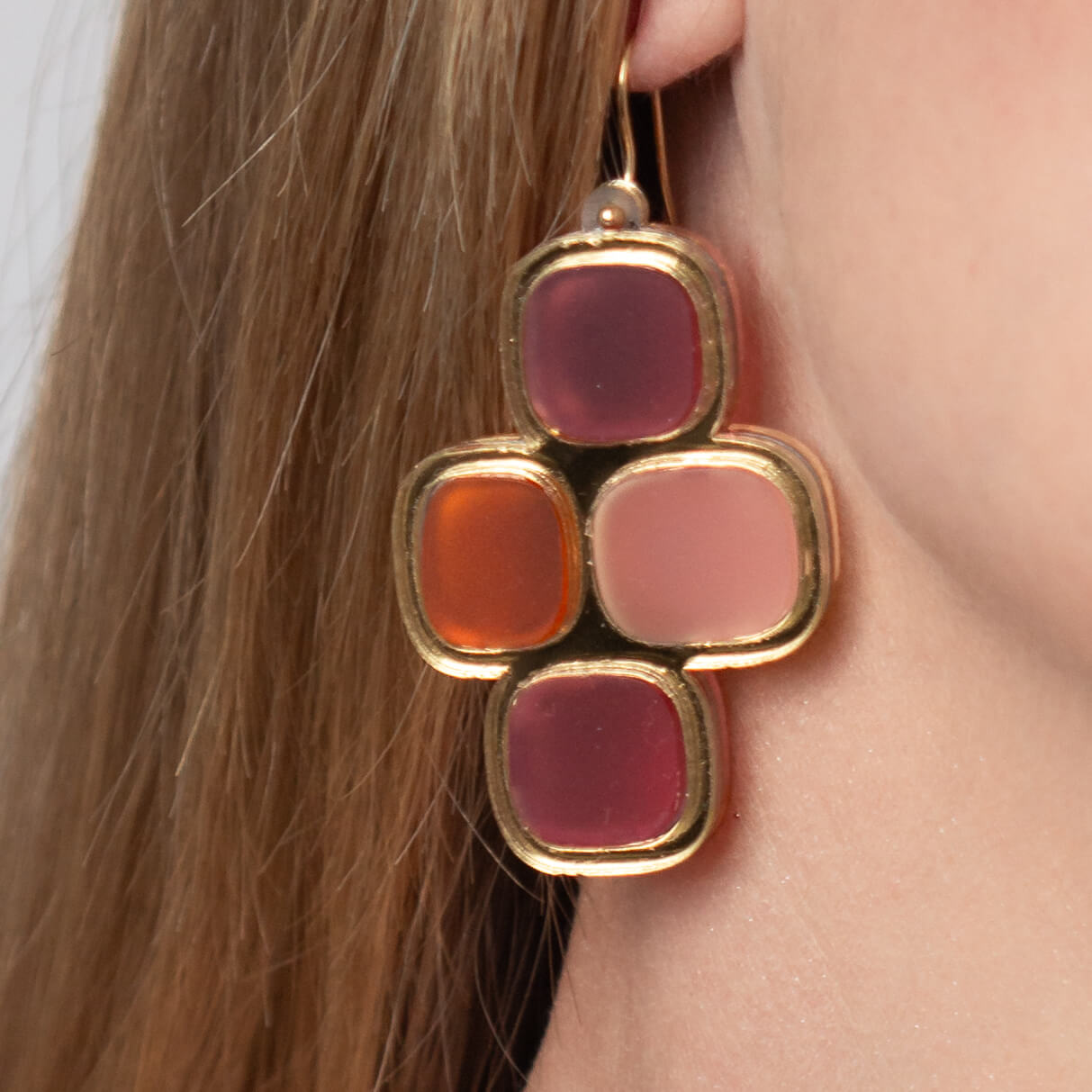Close-up of model’s ear wearing frosted statement wire earrings in gold and summer hues