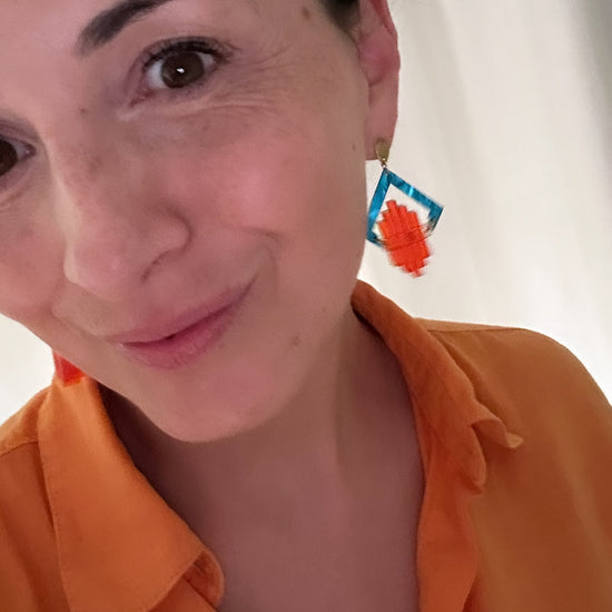 Model wearing turquoise and orange Art Deco Pop earrings with an orange shirt