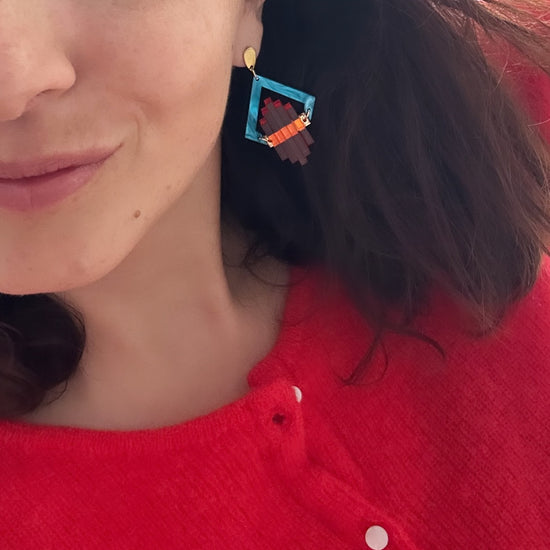 Model wearing turquoise and orange Art Deco Pop earrings with a red cardigan
