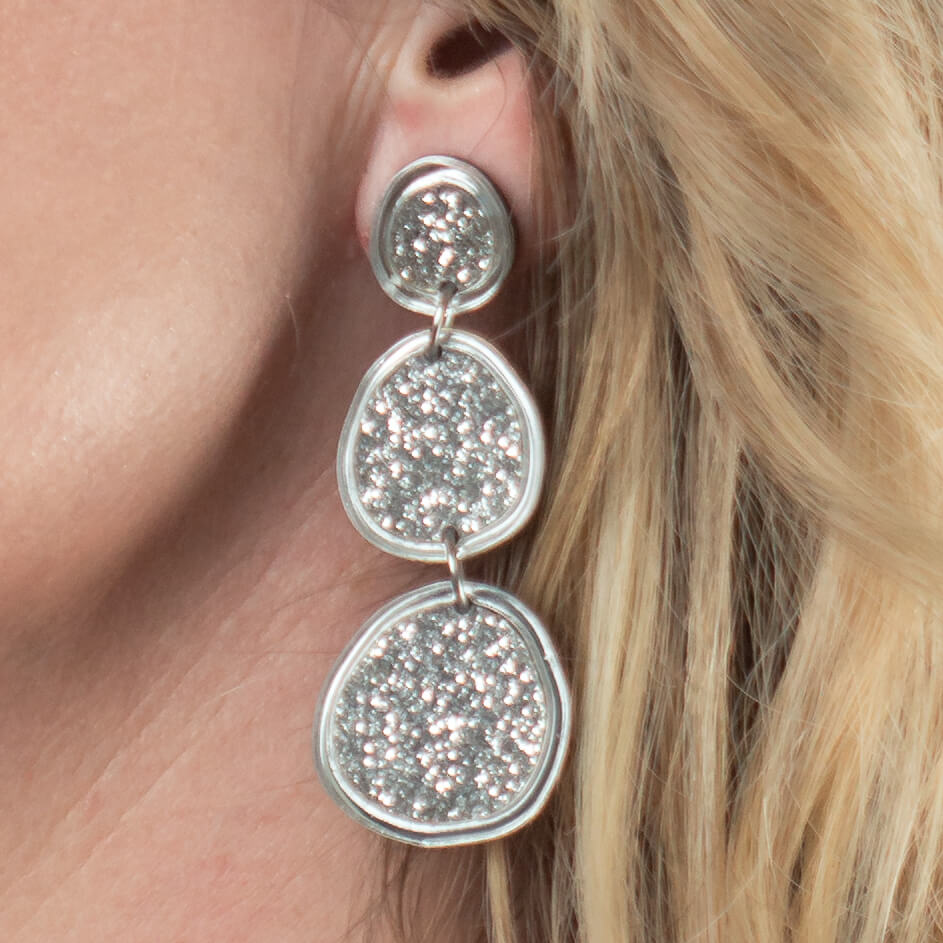 Close-up of model’s ear wearing shimmering silver statement earrings